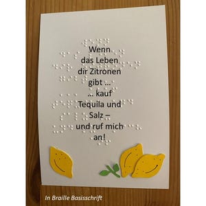 Könnte beinhalten: Weiße Karte mit deutschem Text in Blindenschrift: „Wenn das Leben dir Zitronen gibt... kaufe Tequila und Salz und ruf mich an!“ Gelbe Zitronen-Ausschnitte unten. Text unten: „In Braille Basisschrift“.