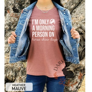 K&ouml;nnte beinhalten: Heather-Mauvefarbenes T-Shirt mit dem wei&szlig;en Text "I'M ONLY A MORNING PERSON ON horse show days". Das Shirt zeigt eine Pferde-Grafik. Das Model tr&auml;gt eine Jeansjacke und blaue Jeans. Das Shirt hat eine Heather-Mauve Farbe.