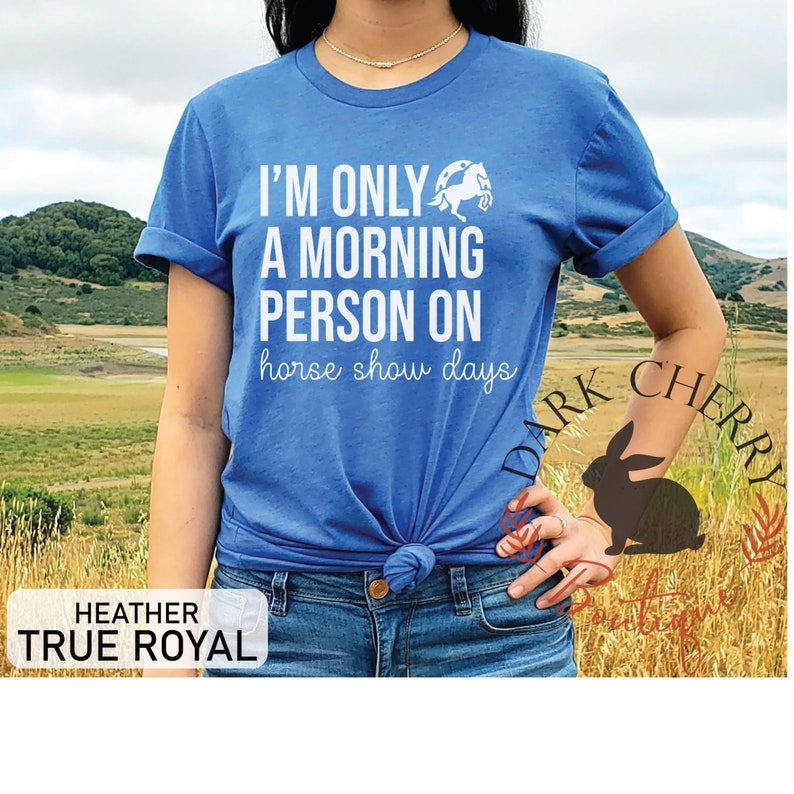 K&ouml;nnte beinhalten: Ein blaues T-Shirt mit wei&szlig;em Text, der "Ich bin nur ein Morgenmensch an Pferdeshow-Tagen" lautet. &Uuml;ber dem Text befindet sich eine wei&szlig;e Silhouette eines Pferdes. Das Shirt wird von einer Person mit blauer Jeans getragen.