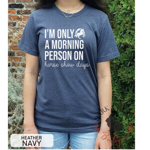 K&ouml;nnte beinhalten: Melierter marineblauer T-Shirt mit dem wei&szlig;en Text "I'M ONLY A MORNING PERSON ON horse show days". Eine wei&szlig;e Pferde-Grafik befindet sich &uuml;ber dem Text. Das T-Shirt hat einen Rundhalsausschnitt.