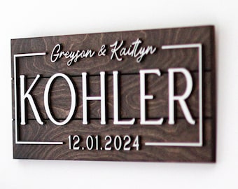 May include: A dark brown wooden sign with white lettering. The sign reads "Greyson & Kaitlyn KOHLER 12.01.2024".
