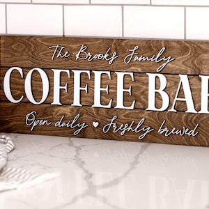 Puede incluir: Un letrero de madera con el texto "The Brooks Family Coffee Bar" en letras blancas. El letrero tambi&eacute;n dice "Open daily  freshly brewed" en letras blancas m&aacute;s peque&ntilde;as.