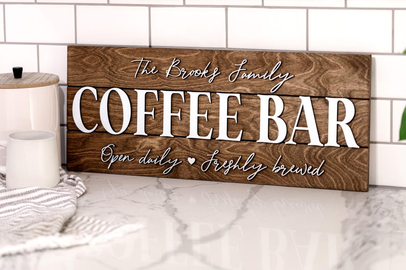 Puede incluir: Un letrero de madera con el texto "The Brooks Family Coffee Bar" en letras blancas. El letrero tambi&eacute;n dice "Open daily  freshly brewed" en letras blancas m&aacute;s peque&ntilde;as.