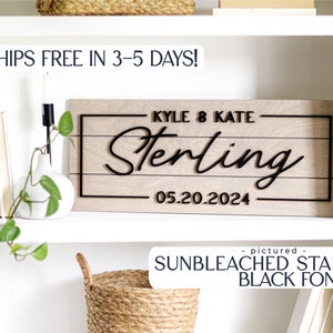 May include: A wooden sign with the text "KYLE & KATE Sterling 05.20.2024" in black lettering. The sign is on a white shelf with a potted plant and a basket.