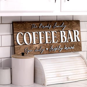 Puede incluir: Un letrero de madera con el texto "The Brooks Family Coffee Bar" en letras blancas. El letrero tambi&eacute;n dice "Open daily &hearts; Freshly brewed".
