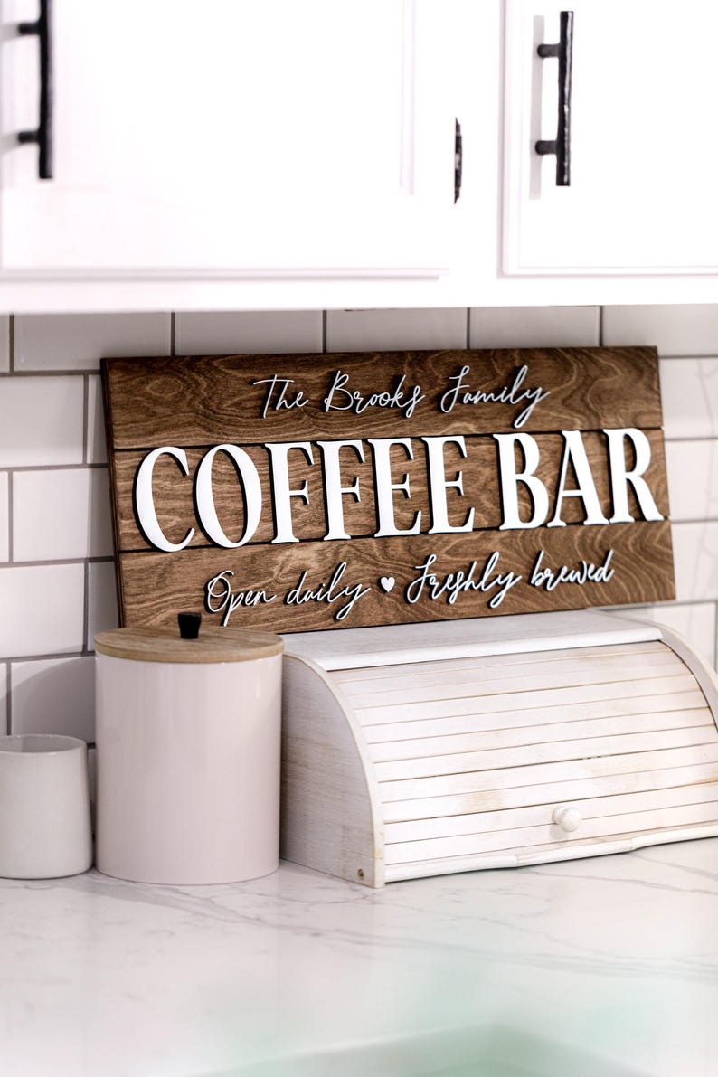 Puede incluir: Un letrero de madera con el texto "The Brooks Family Coffee Bar" en letras blancas. El letrero tambi&eacute;n dice "Open daily &hearts; Freshly brewed".