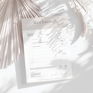 May include: A beige invoice with the word "Rechnung" at the top. The invoice lists two items: "Fotografische Shooting "Begleitend" Paket Silber" and "Laminierte Druck DIN A4". The total amount is 180.00 EUR.
