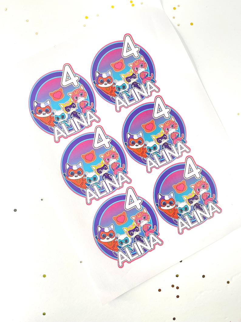May include: Five round stickers with a purple, pink and blue gradient background. Each sticker features a group of cartoon cats wearing superhero costumes. The text "ALINA 4" is printed on each sticker.