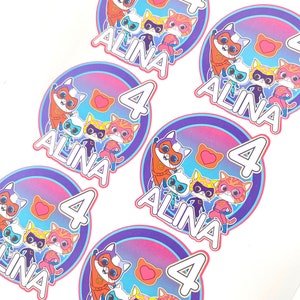 May include: Six colourful round stickers featuring a group of cartoon cats dressed as superheroes. Each sticker includes a pink heart, the number 4, and the name "Alina".
