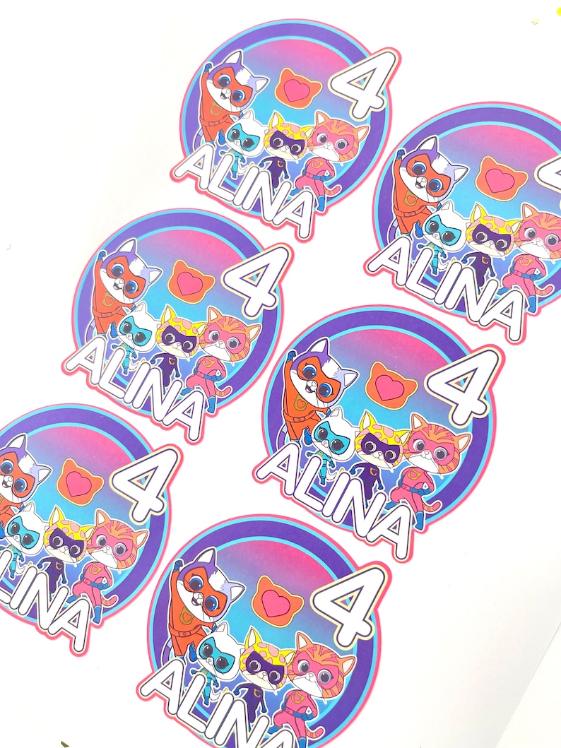 May include: Six colourful round stickers featuring a group of cartoon cats dressed as superheroes. Each sticker includes a pink heart, the number 4, and the name "Alina".