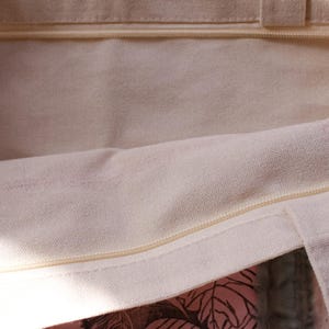 Pu&ograve; includere: Primo piano dell'interno di una borsa tote in tela bianca con chiusura a zip. La borsa non &egrave; foderata e ha un aspetto naturale non sbiancato.