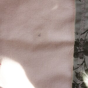 Pu&ograve; includere: Primo piano di un tessuto rosa chiaro con una piccola macchia scura. Il tessuto &egrave; accanto a un tessuto con un motivo floreale in tonalit&agrave; di grigio e verde.