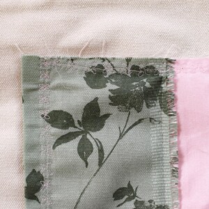 Pu&ograve; includere: Un primo piano di un patchwork di tessuti con una stampa floreale verde e un tessuto rosa con una stampa floreale. Il tessuto verde ha un bordo sfilacciato.