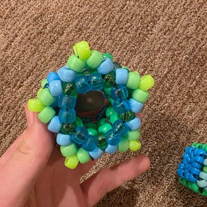 May include: A handmade, five-pointed star-shaped bead creation in shades of blue, green, and yellow. The beads are strung together to form a geometric design. A second, similar bead creation is visible.