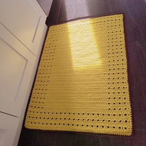 Peut inclure: Un tapis crocheté jaune avec une bordure marron. Le tapis est posé sur un sol carrelé.