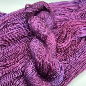 May include: A skein of purple yarn with a subtle iridescent sheen. The yarn is soft and smooth, and it is perfect for knitting or crocheting.