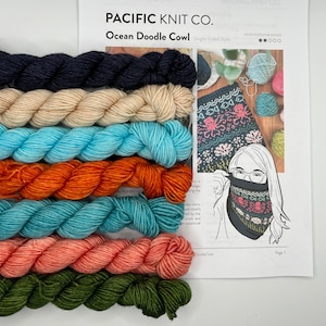 May include: A kit for knitting an Ocean Doodle Cowl, featuring seven skeins of yarn in various shades of blue, orange, green, pink, and beige. The kit includes instructions for knitting a single-sided cowl.