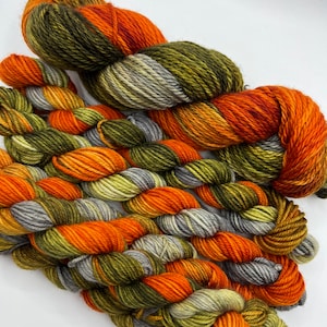 May include: A set of five skeins of yarn in shades of green, orange, and gray. The yarn is arranged in a braided pattern.