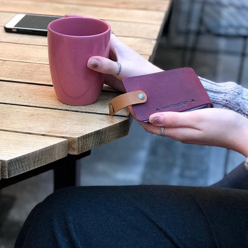 May include: A burgundy leather wallet with a tan leather strap and a silver rivet. The wallet has the text "Raw Rustic" embossed on the front.