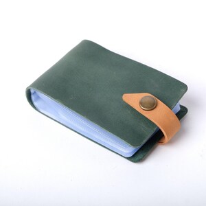 May include: A green leather card holder with a light blue plastic insert and a brown leather strap with a brass button closure.