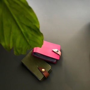 May include: Two leather card holders, one pink and one green, with a snap closure and a strap.