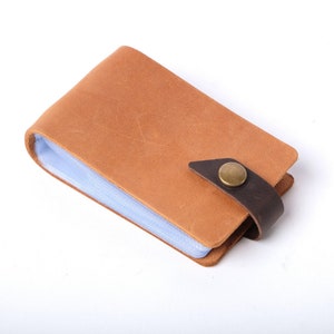 May include: A brown leather card holder with a clear plastic insert and a brown leather strap with a brass button closure.