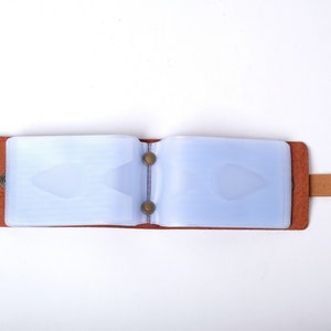 May include: A brown leather card holder with a clear plastic insert for holding cards. The holder has a strap with a metal button.