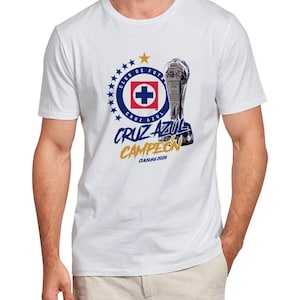 May include: White t-shirt featuring a graphic of the Cruz Azul soccer team logo, a trophy, and the words "Cruz Azul Campeon Clausura 2026" in blue and gold. The logo includes a blue circle with stars, a red cross, and the words "Club de Futbol Cruz Azul".