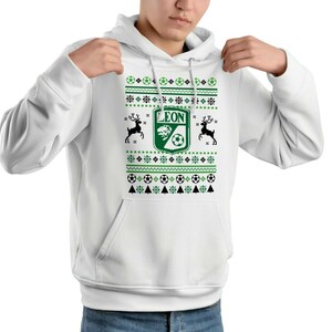 Könnte beinhalten: Weißer Hoodie mit grünem und schwarzem Muster. Das Design umfasst Fußbälle, Schneeflocken und Rentiere. In der Mitte befindet sich ein grünes Wappen mit dem Wort "LEON" und einem Fußball.