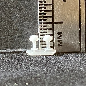 May include: Two white plastic toggle buttons with a small hole in the center of each button. The buttons are about 1/2 inch in diameter and are next to a ruler marked in inches and millimeters.