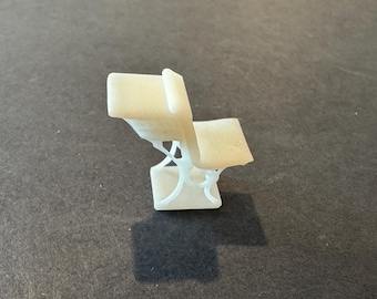 Könnte beinhalten: Ein kleiner, cremefarbener Miniaturstuhl mit einem einzigartigen, durchbrochenen Design. Der Stuhl hat eine Sitzfläche, eine Rückenlehne und eine Basis mit aufwendigen Stützen. Der Stuhl ist wahrscheinlich ein Dekorationsartikel oder ein Modell, das eine moderne Ästhetik zeigt.