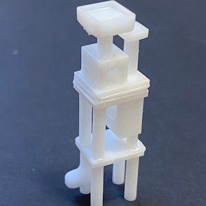 May include: White plastic 3D printed model of a tower with a square platform on top and four legs. The tower has multiple levels with open spaces and a small hole in the center.