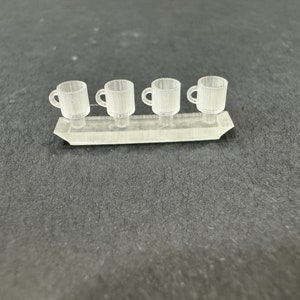 Peut inclure: Quatre tasses miniatures en plastique transparent sur un support en plastique transparent. Les tasses sont toutes de la même taille et de la même forme.