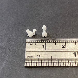 May include: Two white, 3D printed squirrel figurines, approximately 2.5 cm in length, are shown next to a ruler. The ruler is marked in inches and millimetres.