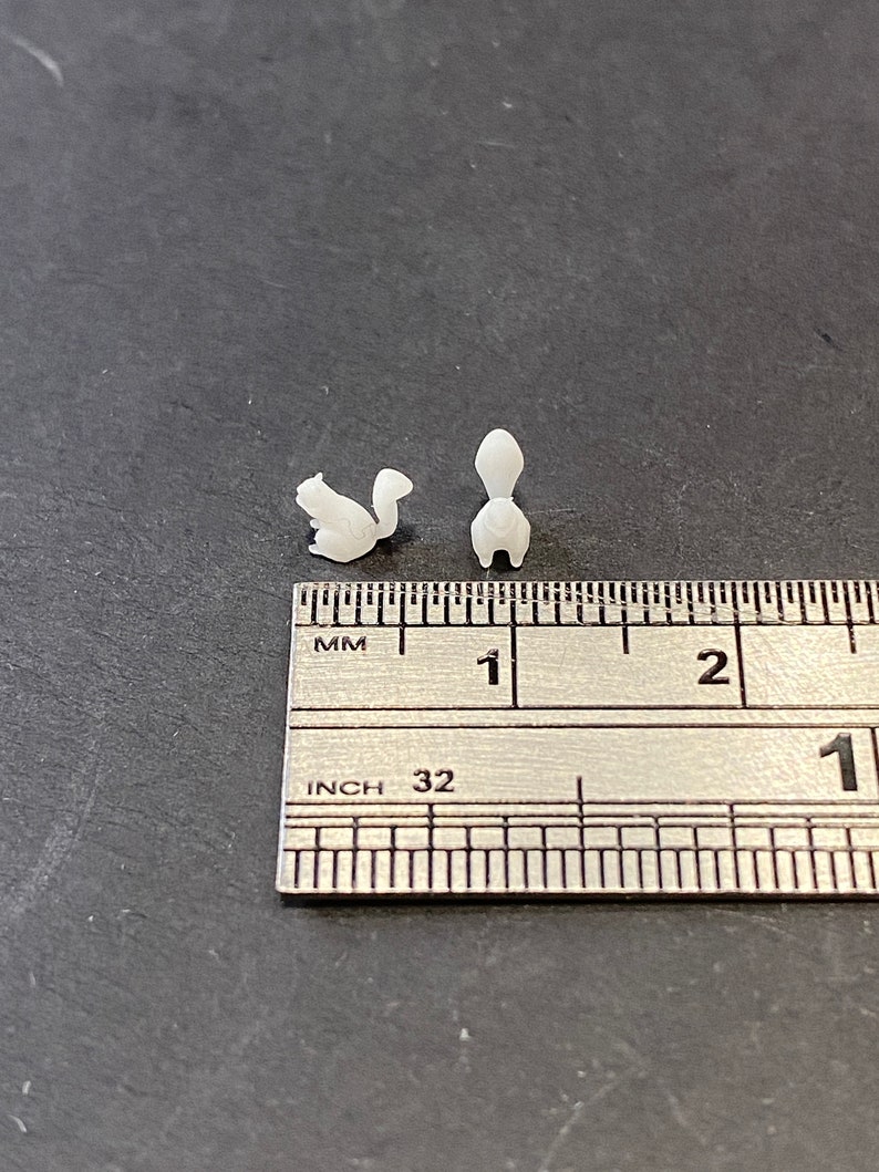 May include: Two white, 3D printed squirrel figurines, approximately 2.5 cm in length, are shown next to a ruler. The ruler is marked in inches and millimetres.