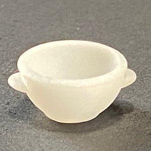 May include: A small, white ceramic bowl with two handles. The bowl is smooth and has a rounded shape.