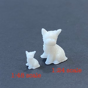 May include: Two white plastic figurines of dogs, one larger than the other. The larger dog is sitting with its head tilted down. The smaller dog is sitting with its head tilted up. The larger dog is labeled "1:24 scale" and the smaller dog is labeled "1:48 scale".