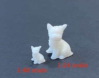 May include: Two white plastic figurines of dogs, one larger than the other. The larger dog is sitting with its head tilted down. The smaller dog is sitting with its head tilted up. The larger dog is labeled "1:24 scale" and the smaller dog is labeled "1:48 scale".