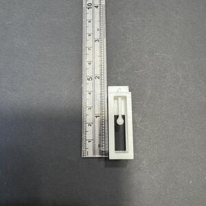 以下が含まれることがあります： 小さな丸いノブが付いた白いプラスチック製のドアストッパー。ドアストッパーの高さは約5cm、幅は約2.5cmです。