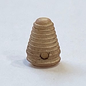 Op de afbeelding: Een klein, beige, keramisch object in de vorm van een bijenkorf met een gat in het midden. Het object is gemaakt van meerdere lagen, die lijken op een bijenkorf.