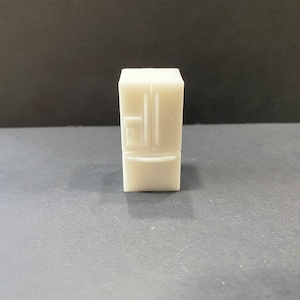 Op de afbeelding: Een klein, crèmekleurig koelkastmodel met een side-by-side deurontwerp. Het miniatuurapparaat heeft een vriesvak aan de onderkant en een waterdispenser. Het algehele ontwerp is rechthoekig en eenvoudig.