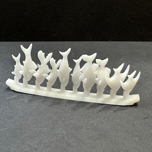 May include: A white plastic sprue with multiple fish-shaped charms attached. The charms are arranged in a row and are ready to be broken off the sprue.