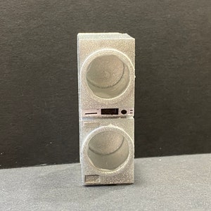 May include: A silver stacked washer and dryer appliance with a black control panel. The appliance has a round door with a clear glass window.