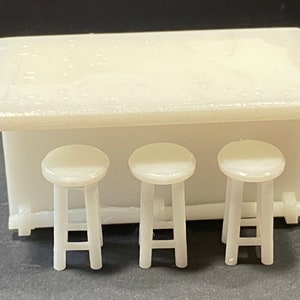 Peut inclure: Comptoir blanc avec trois tabourets blancs. Le comptoir est en plastique et a une surface lisse. Les tabourets sont également en plastique et ont un design simple.