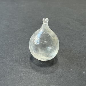 May include: A clear glass bottle with a round body and a narrow neck. The bottle has a textured surface and is empty.