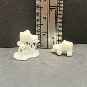 May include: Two white plastic roller skate figurines. One is a traditional roller skate with four wheels. The other is a more abstract design with a shoe on top of three mushroom-shaped supports.
