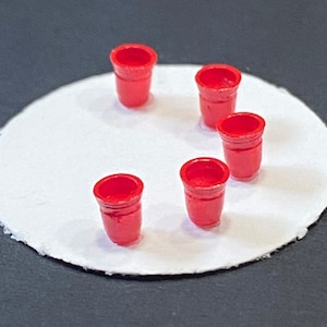 Könnte beinhalten: Fünf rote Plastikbecher, die in einem Kreis auf einer weißen Oberfläche angeordnet sind.