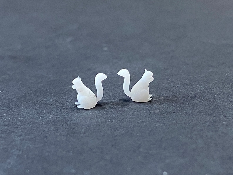 May include: Two white ceramic squirrel figurines facing each other. The squirrels are sitting upright with their tails curled behind them.