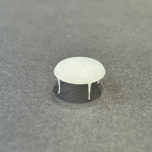 Könnte beinhalten: Ein kleiner weißer Tisch mit runder Tischplatte und vier Beinen. Der Tisch ist aus Kunststoff und hat eine glatte, glänzende Oberfläche.