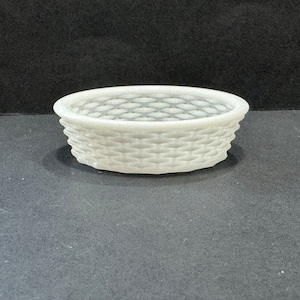 May include: A white ceramic planter with a woven design. The planter has a round shape and a flat bottom.